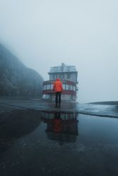 Back view of person in orange jacket standing facing a store on a rainy day