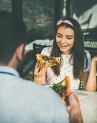 Couple eating pizza al fresco, woman smiling