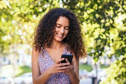 Black Latina woman using a smartphone in the park on a summer day.