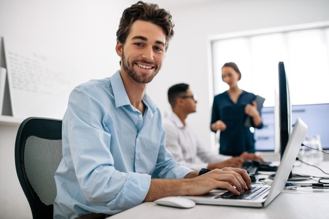 Software developer smiling and looking at camera with colleagues behind