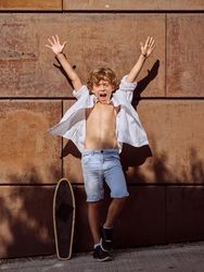 Excited boy with raised arms on street near skateboard