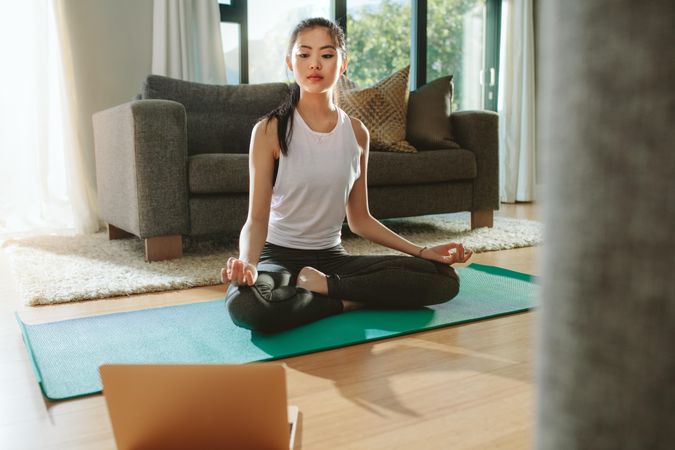 Fit woman doing yoga exercise while watching tutorial on laptop at home