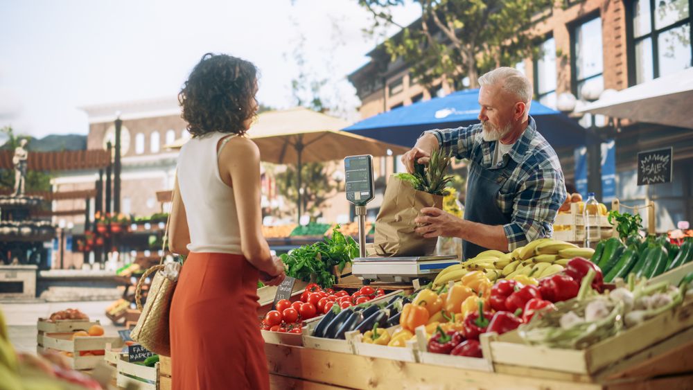 Portrait of a Happy Street Vendor Packing a Paper Bag with Fresh Organic Vegetables for a Female Shopper.