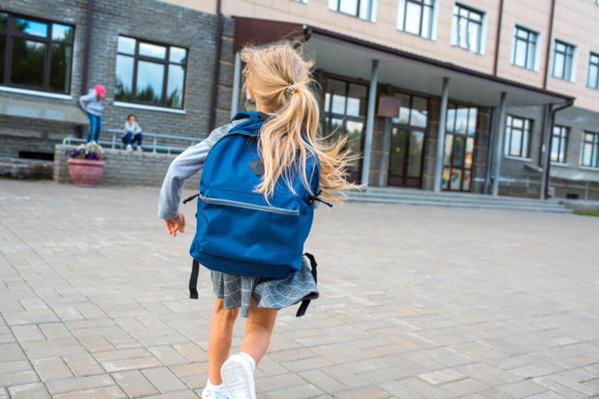 Back view of schoolgirl standing near school