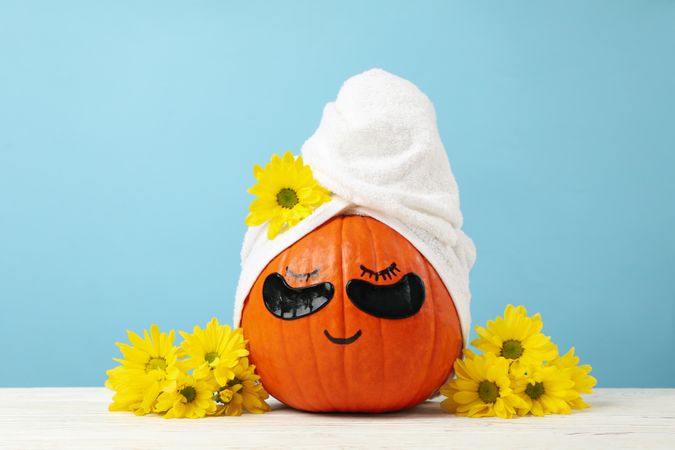 Pumpkin with towel, flowers and under eye patches against blue background