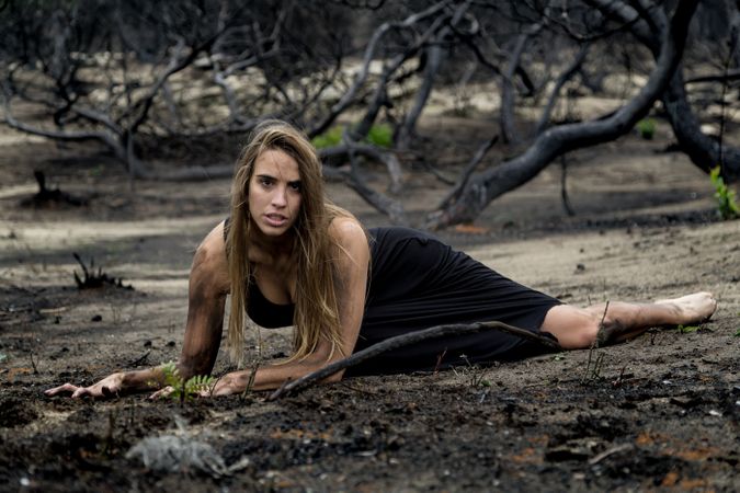 Woman posing on ground near dry trees