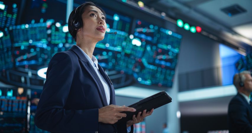 Young Asian Female Broker Working on Tablet Computer on Stock Exchange Floor.