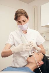 Dentist in mask scanning teeth of woman in dental clinic