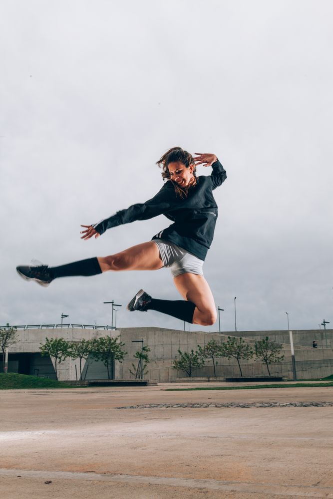 Female dancer in active wear smiling while dancing in jump outdoors