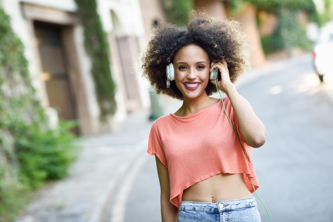 Woman walking down the street wearing orange t-shirt and blue jeans with afro hairstyle