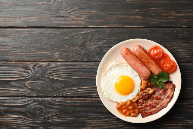Top view of fried breakfast with eggs, bacon and sausage on table, copy space