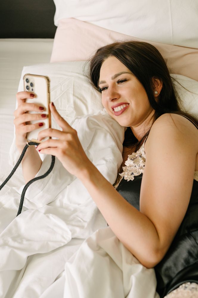 Smiling young woman in bed using smartphone