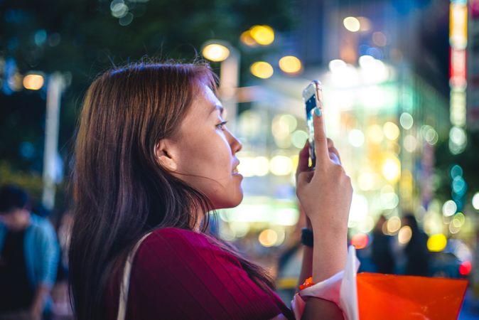Woman taking photo with smartphone in the city during nighttime