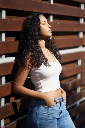 A Stylish Young Woman Posing Gracefully Against a Wooden Fence in the Bright Sunlight