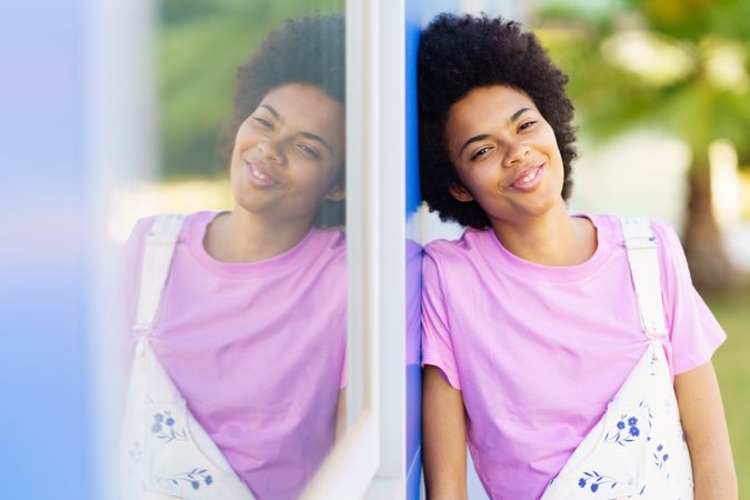 Happy woman looking at camera and leaning her side on blue building