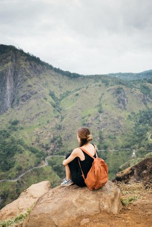 Back of woman sitting on rock taking in view over Sri Lankan hills