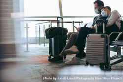 Couple travelers wearing face masks sitting at airport boarding lounge 0Lvgr4