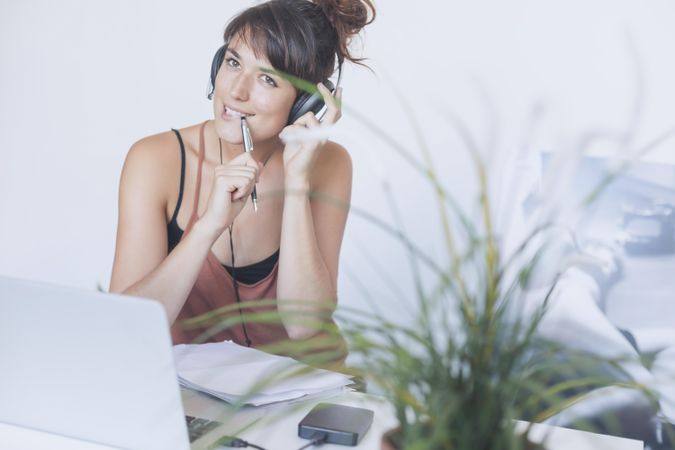 Bemused woman thinking at desk with pen to her mouth