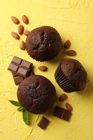 Delicious muffins, chocolate and almond on yellow background