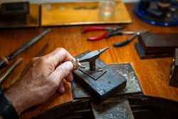 Goldsmith creating and repairing in his crafting gold jewelry workshop with an anvil. Jeweler working in a silver jewel.