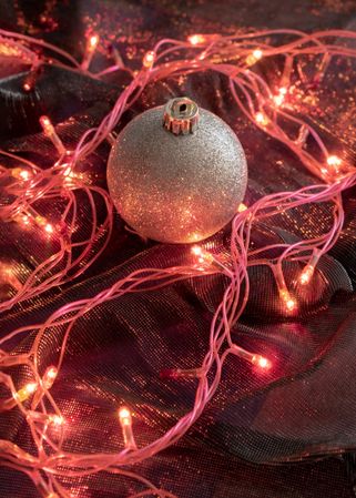 Metallic holiday ornament on red cloth with fairy lights