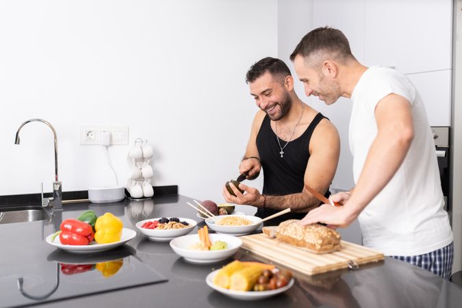 Happy male couple preparing vegetables and cutting bread for lunch in bright kitchen