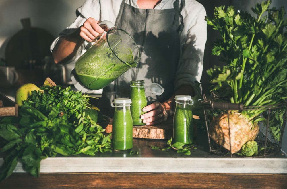 Woman pouring green smoothie from blender into jars in kitchen