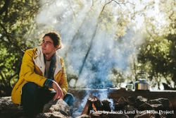 Man on camping trip sitting beside a bonfire in a forest bER1o0