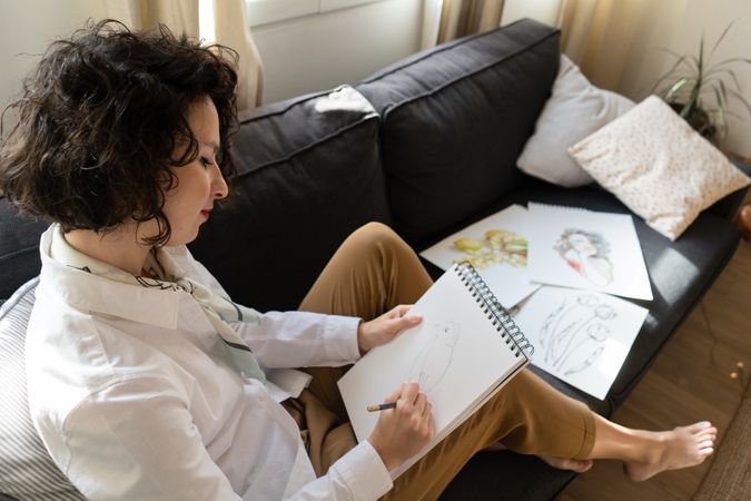 Woman writing on paper on sofa in room