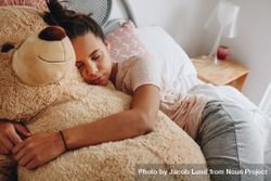 Girl sleeping on bed hugging a brown teddy bear 4NmQl5