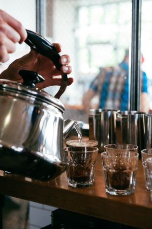 Man’s hands pouring hot water into glasses for coffee tasting