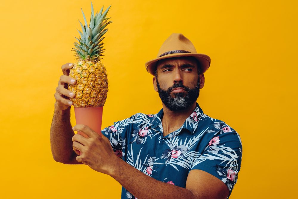 Bemused male holding up a pineapple and orange cup