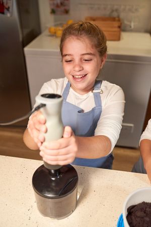 Cheerful girl grinding ingredients in kitchen