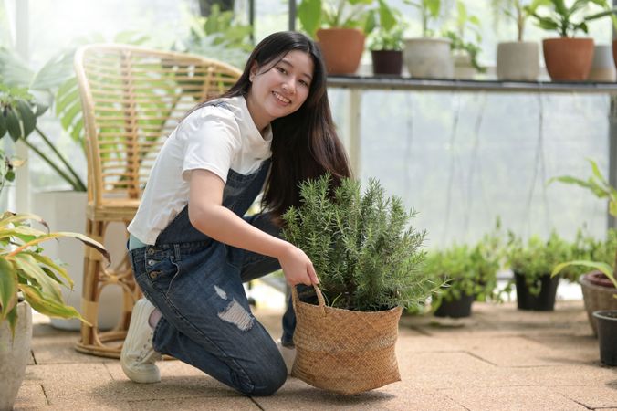 Smiling Asian female tending to a rosemary plant