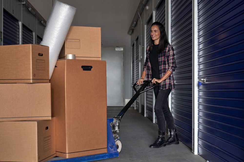 Happy woman using pallet truck to move carton boxes