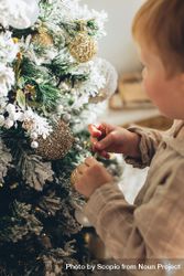 Cropped image of a baby standing beside Christmas tree decorated with gold baubles 0gqAj4