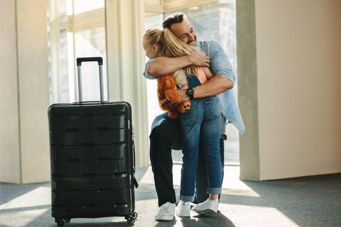 Daughter hugging her father just arrived from a business trip with a travel case