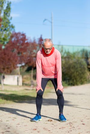 Grey haired man in red shirt and glasses looking down catching his breath between exercising