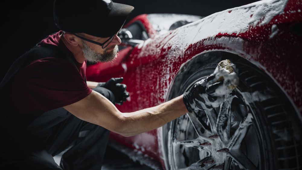 Red Sportscar's Wheels Covered in Shampoo Being Rubbed by a Soft Sponge at a Stylish Dealership Car Wash.