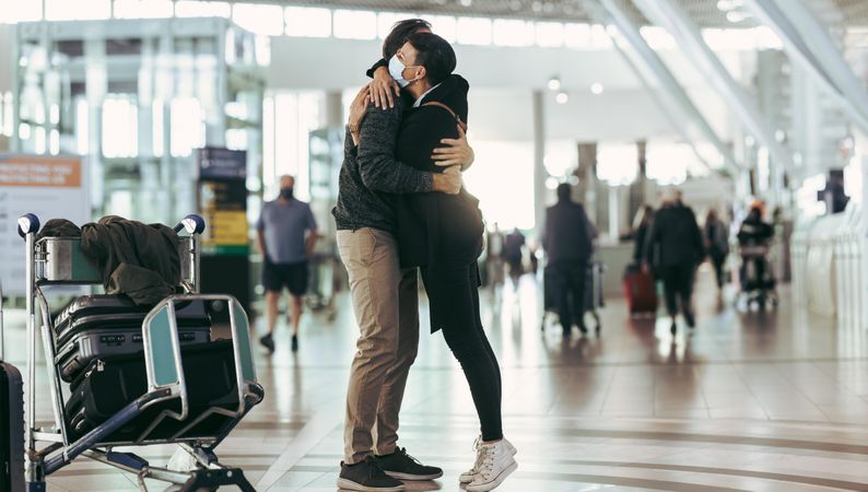 Woman in face mask receiving man at airport arrival
