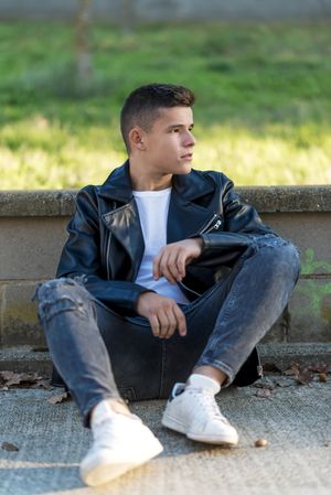 Teenage male wearing a leather jacket leaning on ledge outside