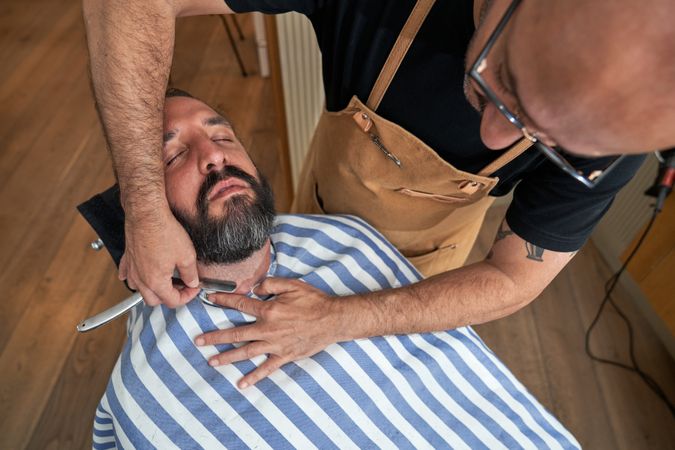 Crop barber trimming beard of client