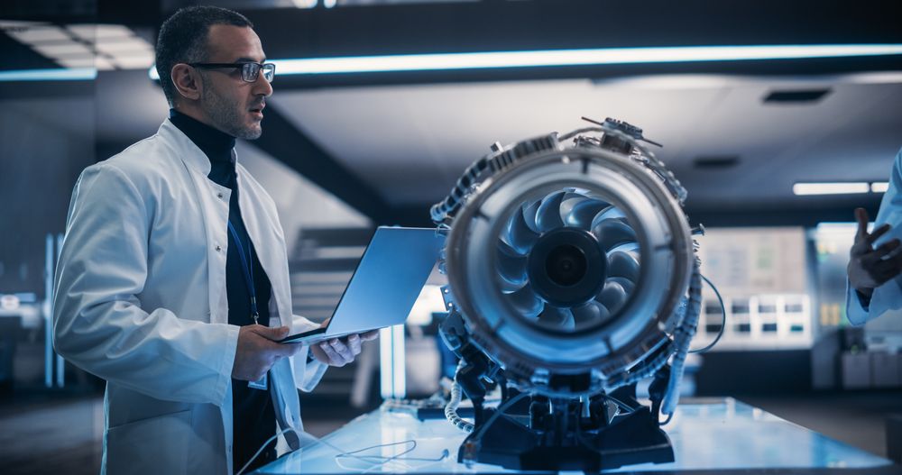 Male Project Leader Holding a Laptop Computer and Explaining the Innovative Technology in Scientific Technology Lab