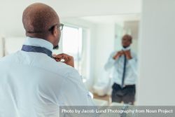 Man putting on a tie looking at a mirror 4OeMJ0