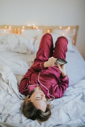 Woman lying down on bed with smartphone