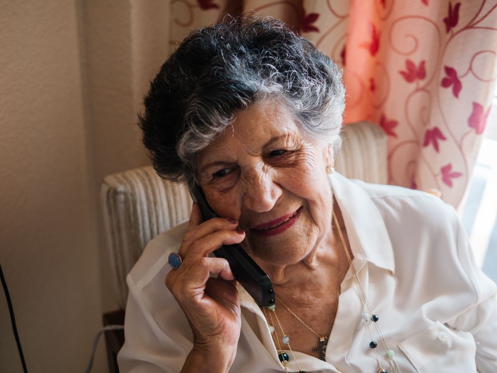 Cheerful mature woman talking on cell phone at home
