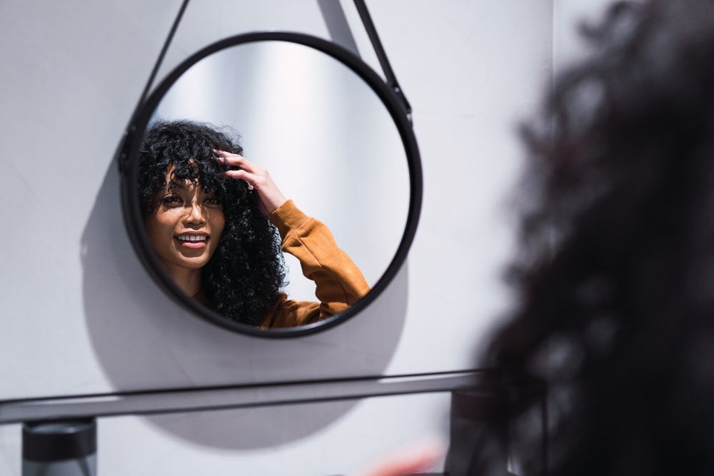 Smiling Black woman looking at mirror at home