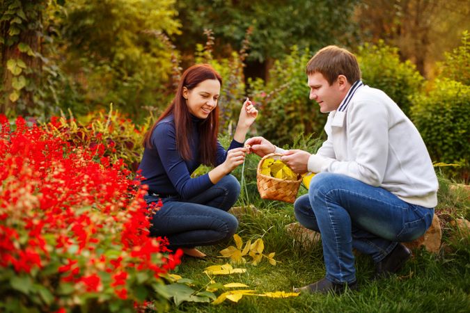 Man and woman sitting in park collecting autumn leaves