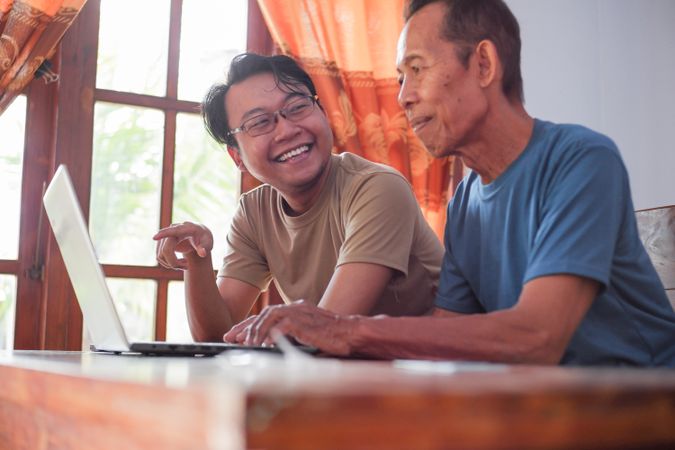Happy adult son teaching mature father using laptop