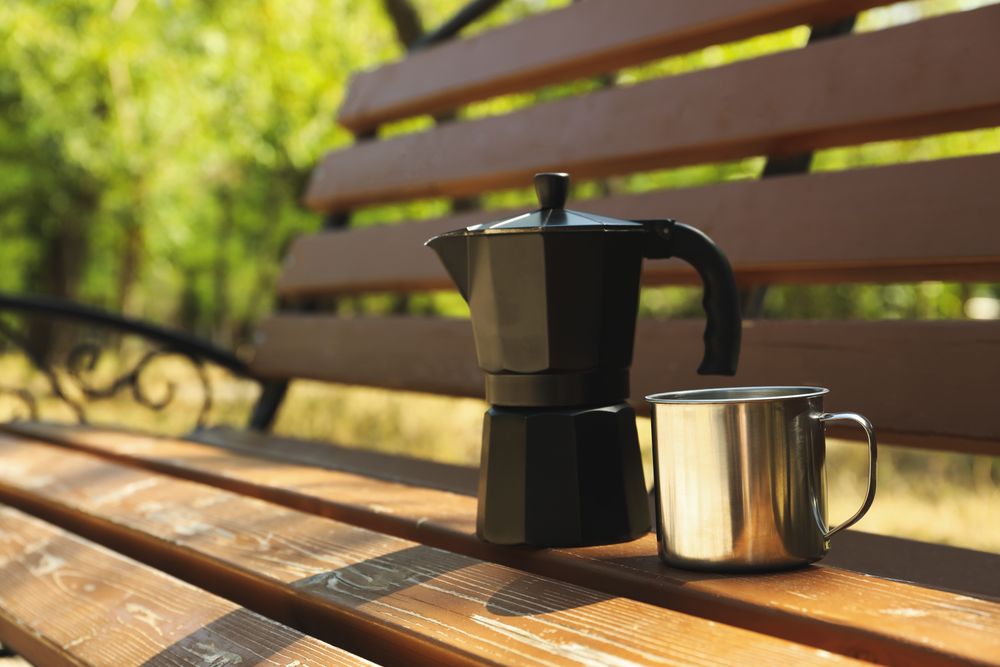 Coffee maker and metal cup on bench outdoor